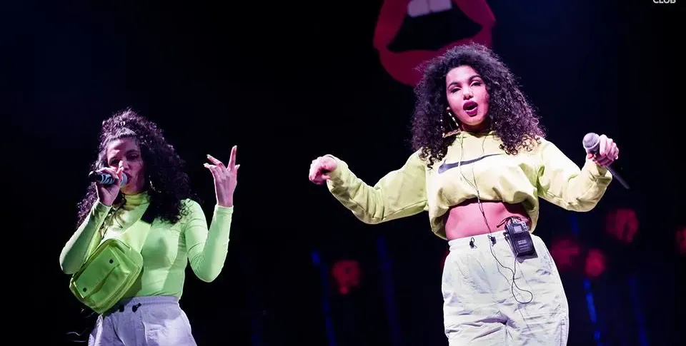 Едната близначка пее с чанта на гърдите